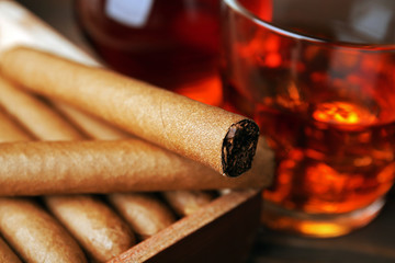 Cigars with glass of cognac on wooden table, closeup
