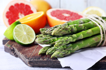 Fresh asparagus and grapefruit on cutting board on color wooden background