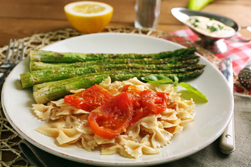 Roasted asparagus and tasty pasta with vegetables on plate on wooden table background
