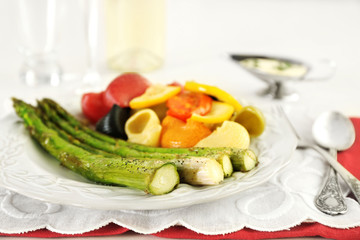 Roasted asparagus and tasty colorful pasta with vegetables on plate on wooden table background