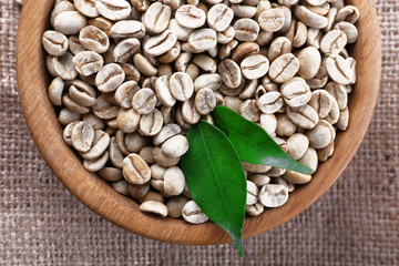 Wooden bowl of green coffee beans on sackcloth, closeup