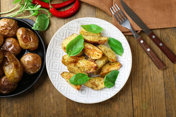 Baked potatoes with basil leaves in white plate on wooden table, top view