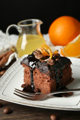 Portion of Cake with Chocolate Glaze and orange on plate, on table, on dark background