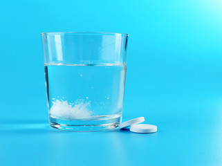 Glass of water and pills on blue background
