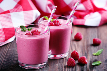 Glasses of raspberry milk shake with berries on wooden table close up
