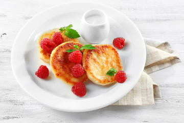 Fritters of cottage cheese with raspberries in plate on table, closeup