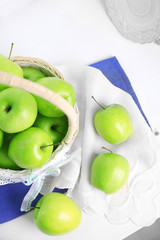 Green apples in wicker basket on table with napkin, closeup