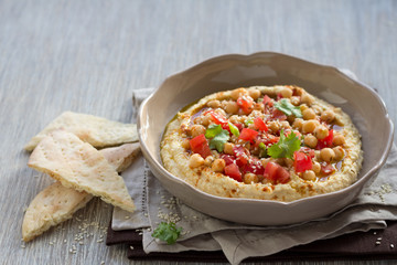 Hummus with a salad of tomato, onion and cilantro on a wooden surface