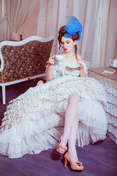 Indoors shot in the Marie Antoinette style. Woman drinking tea with sweets.