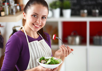 Young woman eating fresh salad in modern kitchen