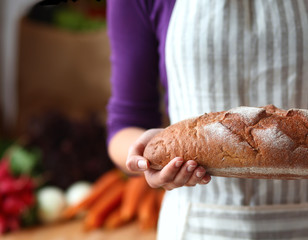 Young woman holding tasty fresh bread in her kitchen