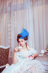 Indoors shot in the Marie Antoinette style. Woman drinking tea with sweets.