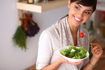 Young woman eating fresh salad in modern kitchen