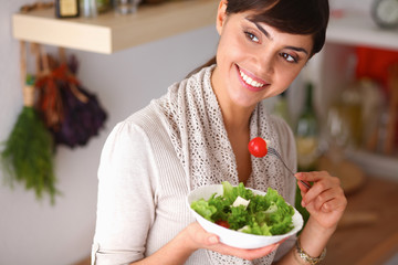 Young woman eating fresh salad in modern kitchen