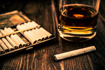 Glass of whiskey and cigarette with a cigarette case on a wooden table