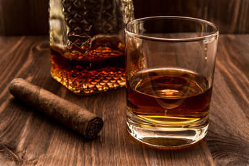 Decanter of whiskey and a glass with cuban cigar on a wooden table