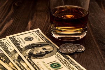Glass of whiskey with money on a wooden table