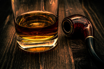 Glass of whiskey and tobacco pipe on a wooden table