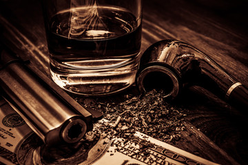 Glass of whiskey and revolver with a money and tobacco pipe on a wooden table © Georgii Shipin
