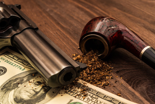 Money and a gun with a pipe on a wooden table