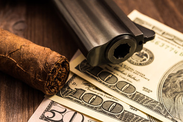 Barrel of a revolver with cuban cigar and money on the wooden table