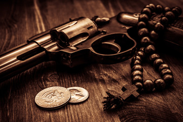 Revolver with coins and a rosary on the wooden table