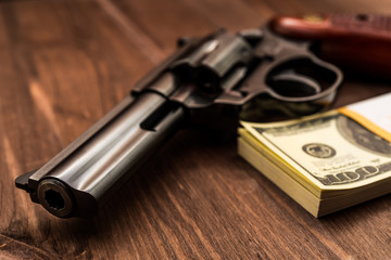 Revolver and pack of dollars on the wooden table