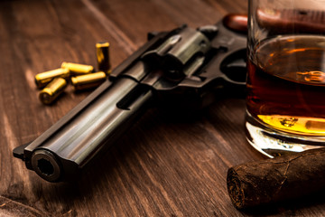 Glass of whiskey with revolver and cuban cigar on the wooden table