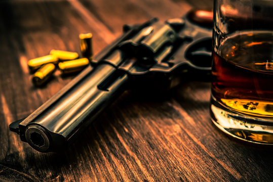 Glass of whiskey with revolver on the wooden table