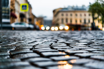City central square paved with stone after a rain, headlights fr