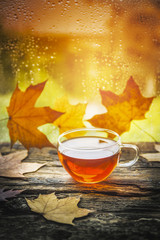 cup of tea on a wooden window sill with autumn leaves against the window with raindrops 