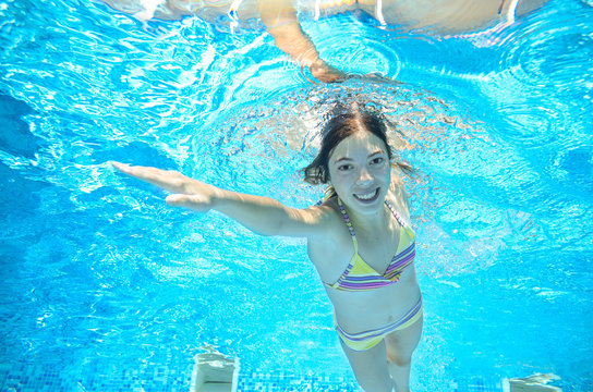 Child swims in pool underwater, happy active girl has fun in water