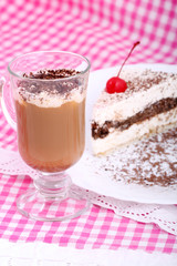 piece of chocolate cake on white plate and cappuchino on checkered table-cloth

