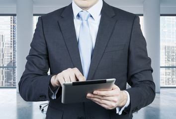 Close-up of the front view of a businessman who is browsing on his tablet. Modern panoramic office...