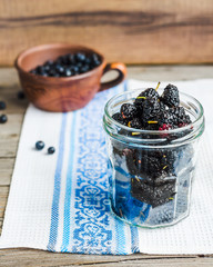 Obraz na płótnie Canvas Fresh black mulberries in a glass jar on the gray wooden backgro