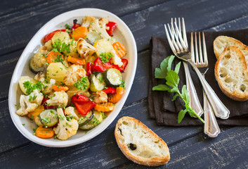 roasted vegetables - zucchini, cauliflower, potatoes, carrots, onions, peppers, on an oval dish on dark wooden background