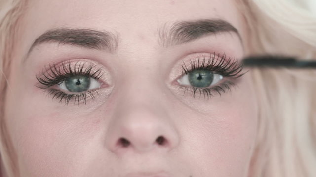 Eye in macro footage of young woman applying mascara on eyelashes