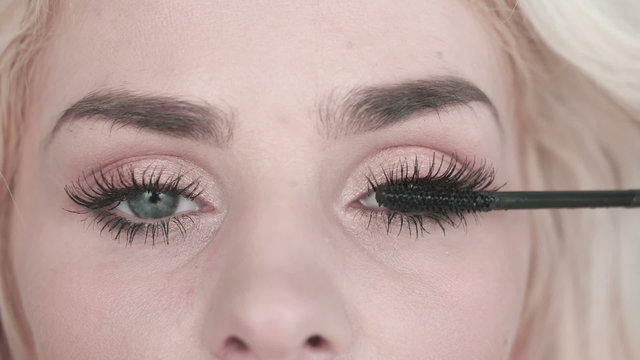 Eye in macro footage of young woman applying mascara on eyelashes