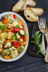 roasted vegetables - zucchini, cauliflower, potatoes, carrots, onions, peppers, on an oval dish on dark wooden background