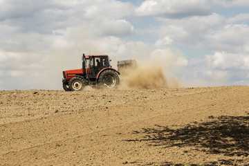 Obraz premium Tractor ploughing a field with a trail of dust behind it