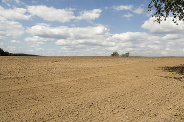 Obraz premium Tractor ploughing a field with a trail of dust behind it