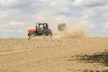 Obraz premium Tractor ploughing a field with a trail of dust behind it