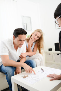 happy young couple at home with blueprint in discussion with a business woman