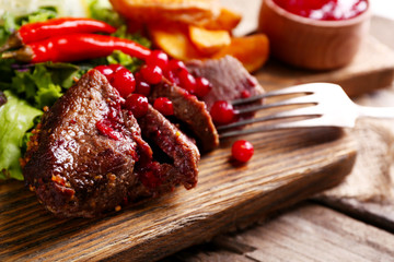 Beef with cranberry sauce, roasted potato slices on cutting board, on wooden background