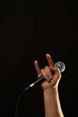 Hand with microphone and devil horns isolated on black