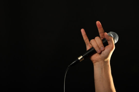 Hand with microphone and devil horns isolated on black