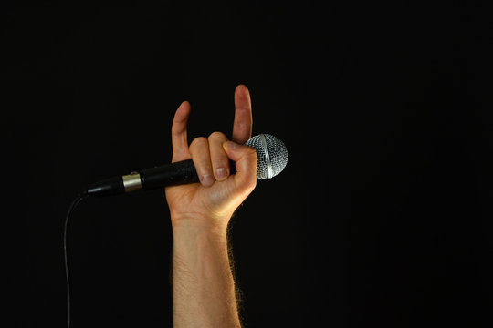 Hand with microphone and devil horns isolated on black