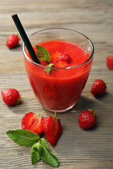 Glass of strawberry smoothie with berries on wooden table close up