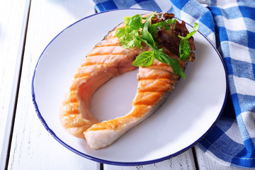Tasty grilled salmon with greens on table close up