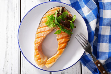 Tasty grilled salmon with greens on table close up